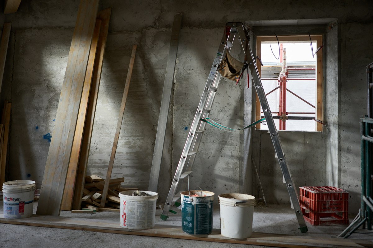 Chantier de second œuvre avant peinture : murs en béton brut, escabeau et seaux de peinture